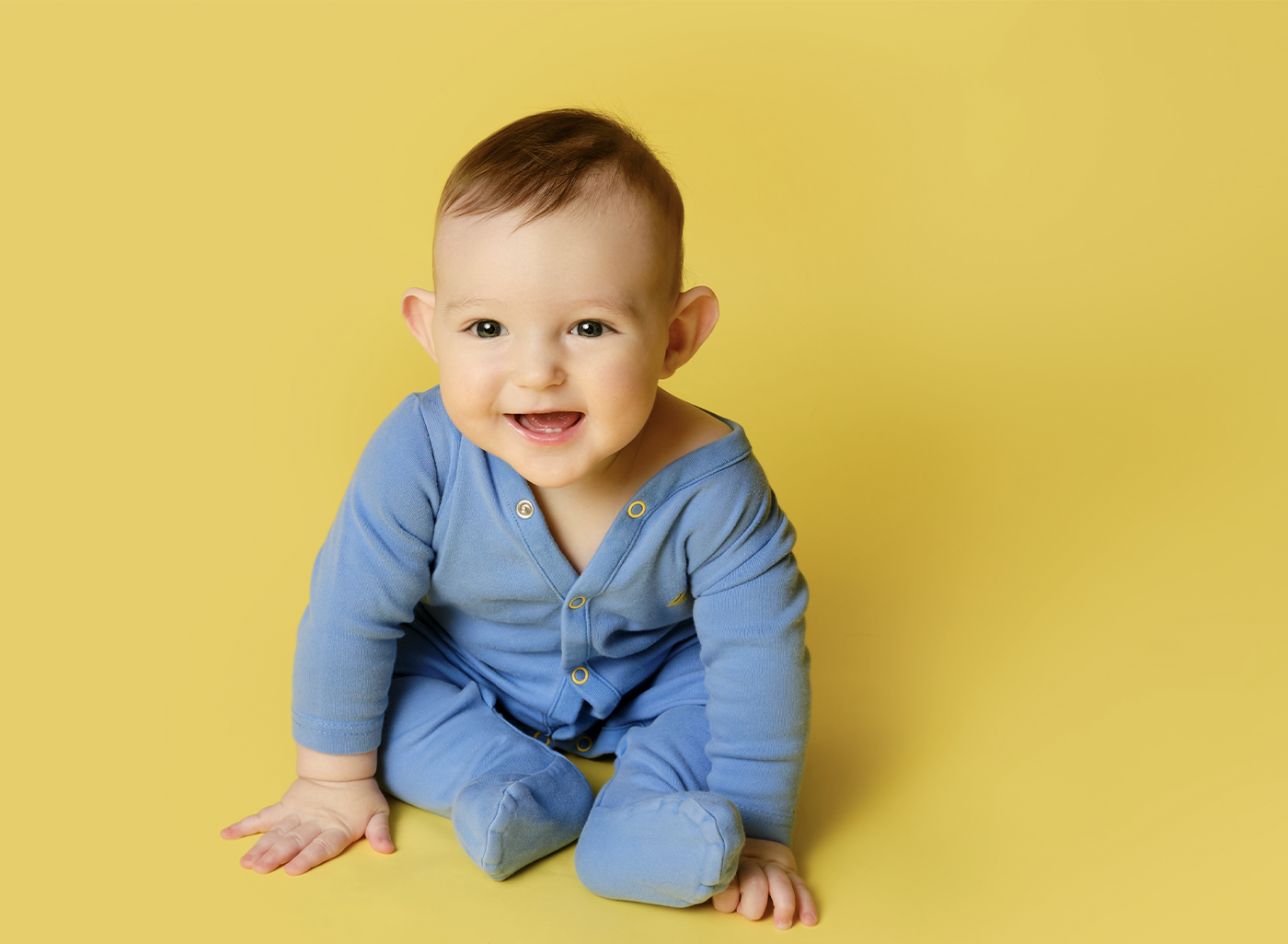 Healthy smiling baby in blue outfit representing successful laser frenectomy for tongue and lip tie treatment